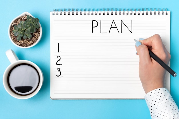 Photo girl writes goals 2021 in notebook on a blue background top view