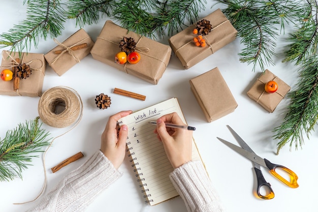 Girl writes her wishes in a Notepad around the Christmas tree and Packed gifts