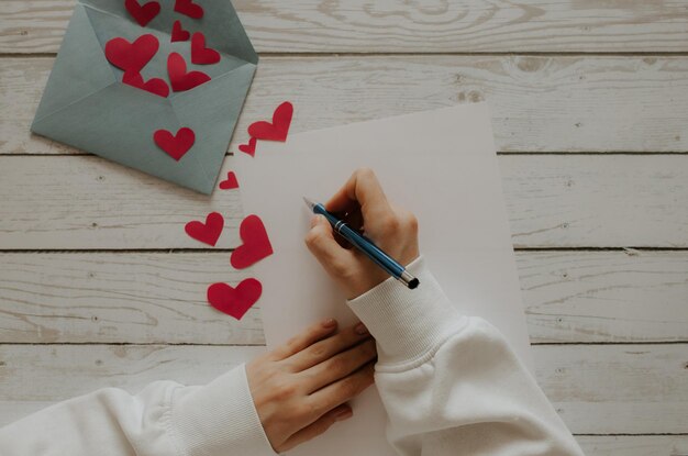 Foto la ragazza scrive una lettera. busta con cuori rossi su fondo di legno.