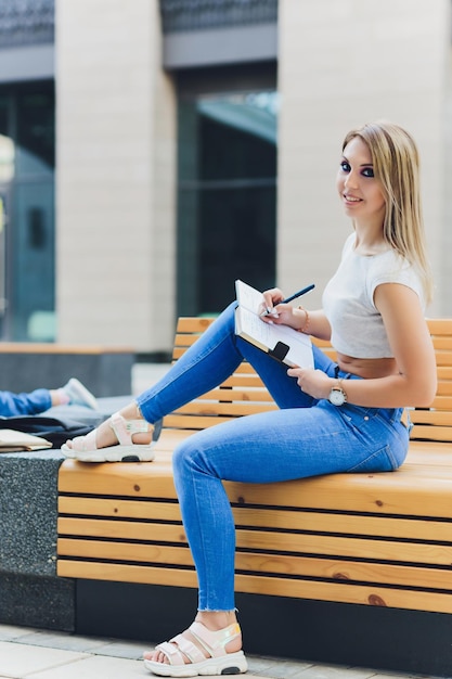 girl writes in a notebook sitting on a bench in the Park