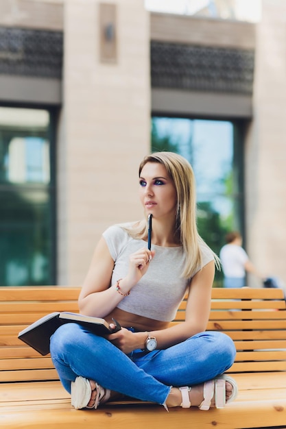 girl writes in a notebook sitting on a bench in the Park