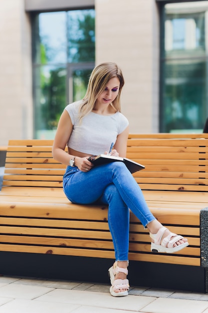 Ragazza scrive su un quaderno, seduto su una panchina nel parco.