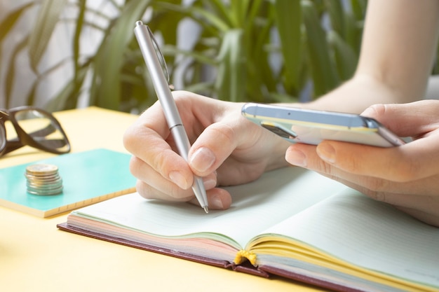 Girl Writes In A Notebook, With Cell Phone And Cup Of Coffee