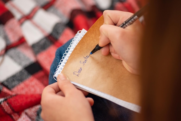 Girl writing letter for Santa Claus sitting on the bed