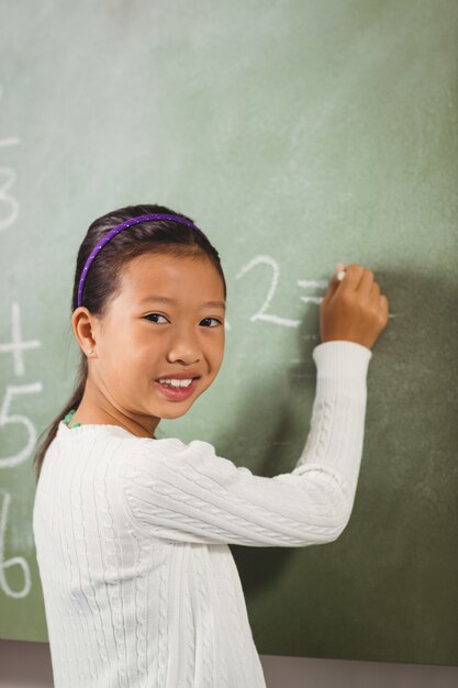 Girl writing with chalk on blackboard