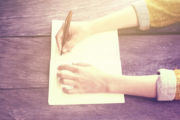 Photo girl writing with pen in blank diary on wooden table instagram photo effect