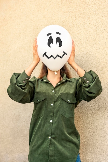 Girl in yard holding inflatable balloon with an evil face in\
her hands outside