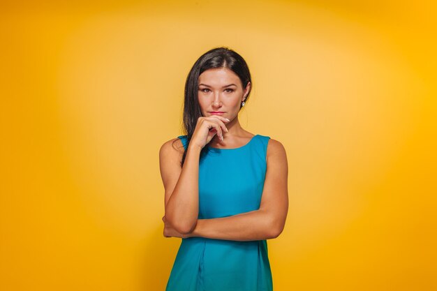 Girl on a yellow background in a blue dress holding her hand to her face