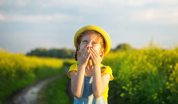 Girl in yellow blooming field covered her nose and face with hands and wrinkled up - an unpleasant smell, irritation, allergy. Allergic reaction to flowering in spring and summer, mosquito repellent