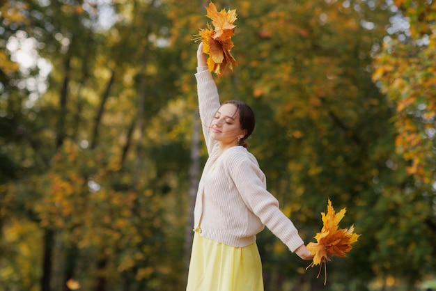 Girl in yellow clothes in autumn park rejoices in autumn holding yellow leaves in her hands warm