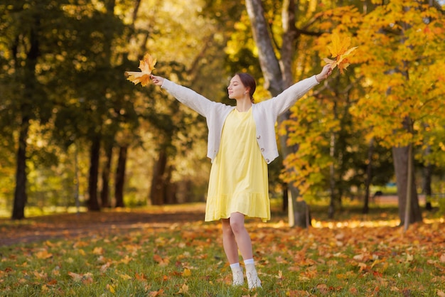 Girl in yellow clothes in autumn park rejoices in autumn\
holding yellow leaves in her hands warm