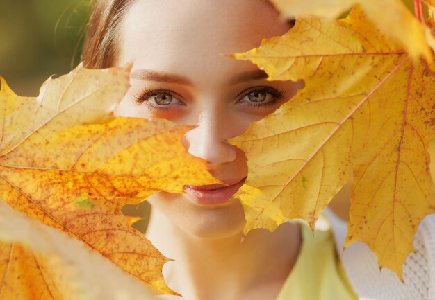 Girl in yellow clothes in autumn park rejoices in autumn
holding yellow leaves in her hands warm