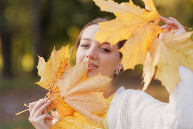 Girl in yellow clothes in autumn park rejoices in autumn holding yellow leaves in her hands warm