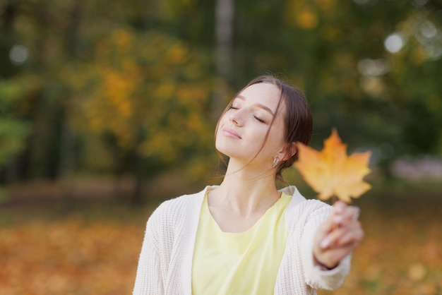 Girl in yellow clothes in autumn park rejoices in autumn
holding yellow leaves in her hands warm