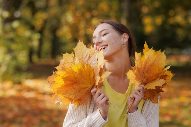 Girl in yellow clothes in autumn park rejoices in autumn\
holding yellow leaves in her hands warm