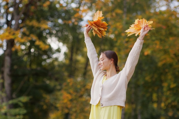 Girl in yellow clothes in autumn park rejoices in autumn holding yellow leaves in her hands warm