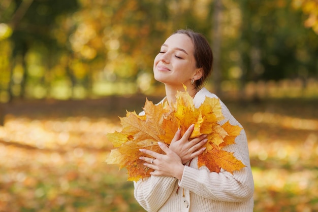 Girl in yellow clothes in autumn park rejoices in autumn holding yellow leaves in her hands warm
