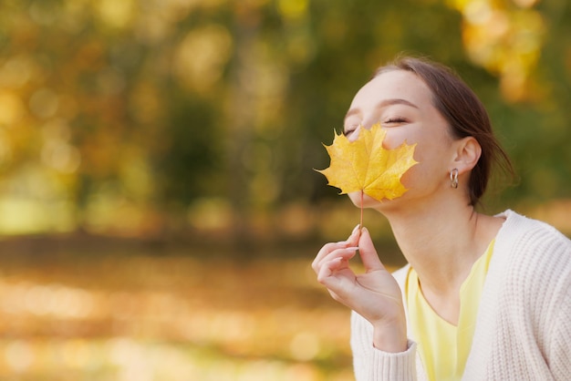 Girl in yellow clothes in autumn park rejoices in autumn\
holding yellow leaves in her hands warm