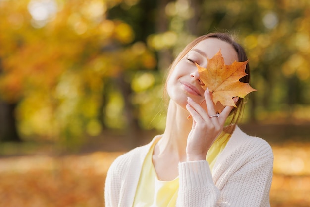 가을 공원에서 노란 옷을 입은 소녀는 손에 노란 잎사귀를 들고 가을에 기뻐한다