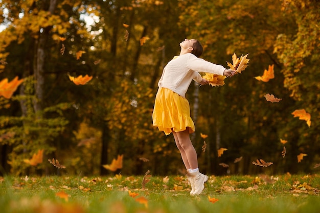 a girl in yellow clothes in an autumn park rejoices in autumn holding yellow leaves in her hands