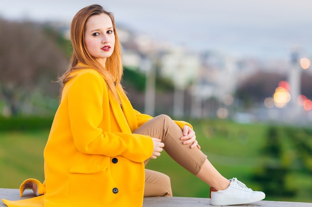 A girl in a yellow coat looks at the camera and poses against th