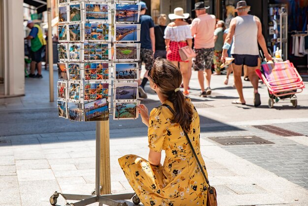 A girl in a yellow dress examines postcards on a stand
