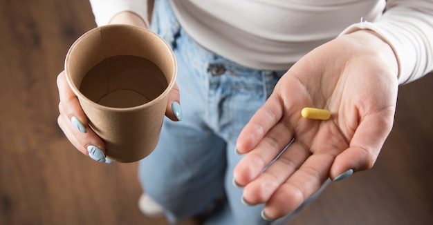 A girl in a yellow dress holds a pill and a glass of water