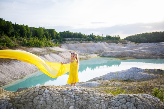 Ragazza in un vestito giallo con le ali in un panno giallo vicino al lago