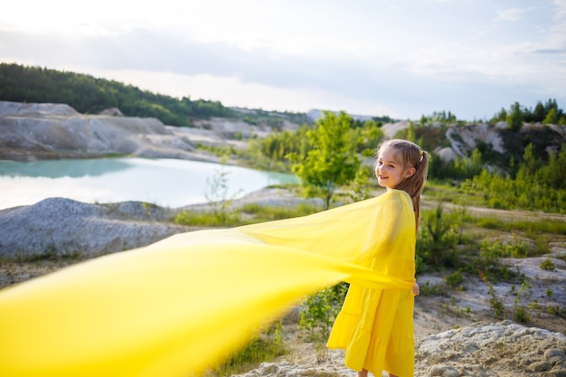 Девушка в желтом платье с крыльями в желтой ткани у озера