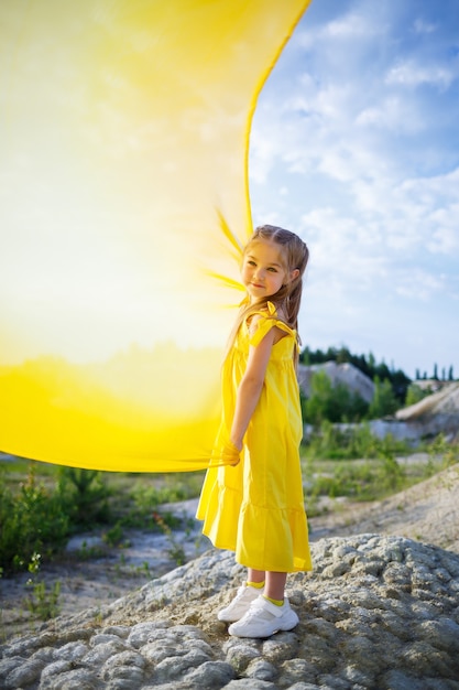 Girl in a yellow dress with wings in a yellow cloth near the lake