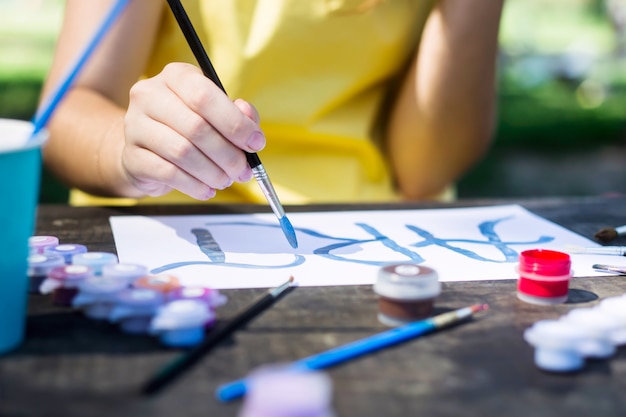 黄色のドレスを着た女の子が一枚の紙にアートという言葉を描きます。木製のテーブルの上。クリエイティブな趣味の概念