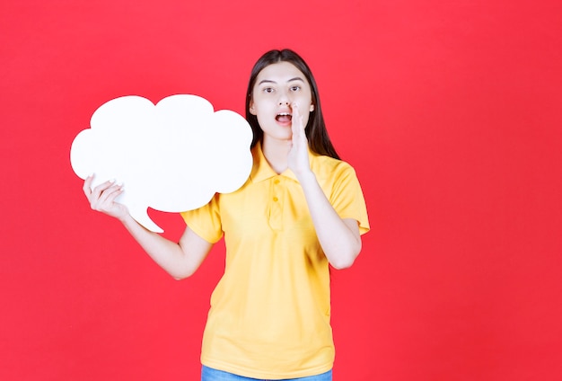 Girl in yellow dresscode holding a cloud shape info board and inviting someone next to her.