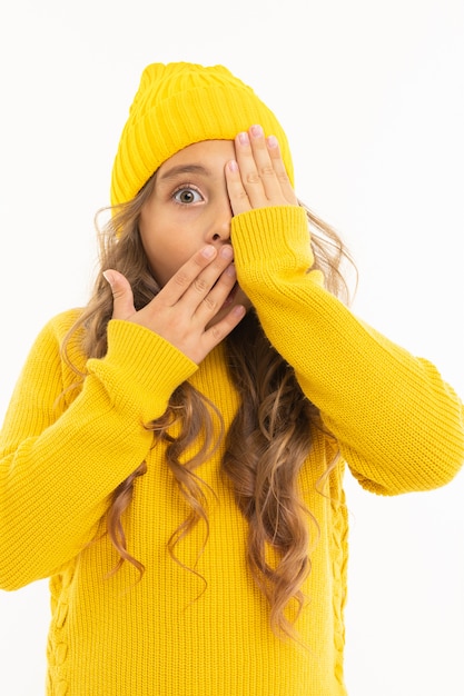 девушка в желтой шапке и пиджаке закрыла лицо руками, лицо и рот на белом