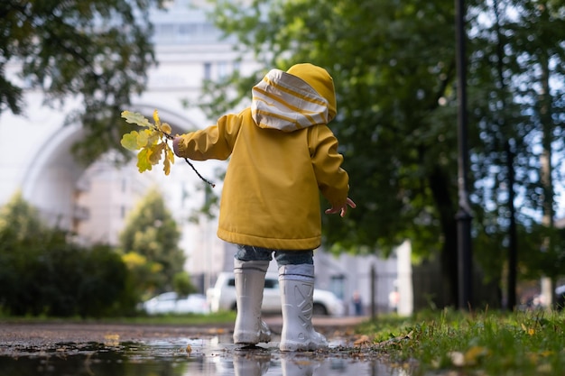 Girl in yellow jacket and white rubber boots is running over a puddle