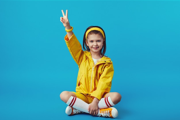 Girl in yellow outfit shows peace gesture while sitting cross legged