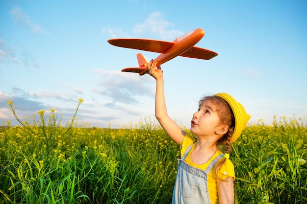 Girl in a yellow panama hat launches a toy plane into the field Summer time happy childhood dreams and carelessness Air tour from a travel agency on a trip flight adventure and vacation