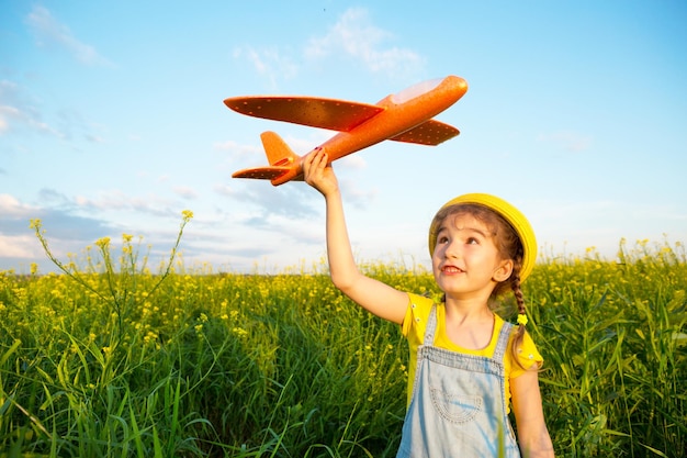 Girl in a yellow panama hat launches a toy plane into the field Summer time happy childhood dreams and carelessness Air tour from a travel agency on a trip flight adventure and vacation