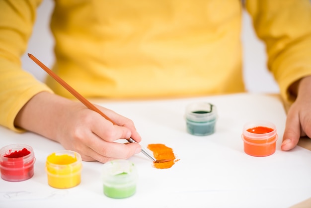 Girl in yellow pullover making picture with gouache paints.