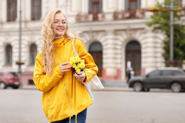 Girl in yellow raincoat with flowers in the city on a walk