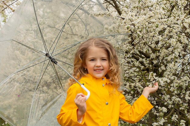 Una ragazza con un impermeabile giallo e con un ombrello in mano vicino a un ramo primaverile in fiore