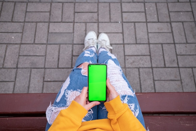 Girl in a yellow sweater holding a phone with a green screen