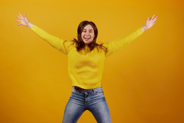 Girl in a yellow sweater rejoices on a yellow background