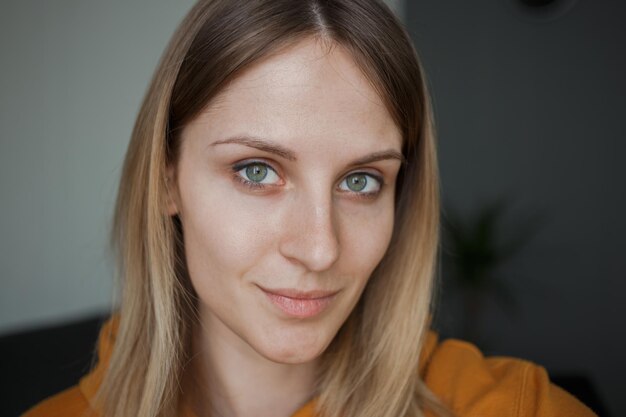 A girl in a yellow sweatshirt with green eyes looks at the camera