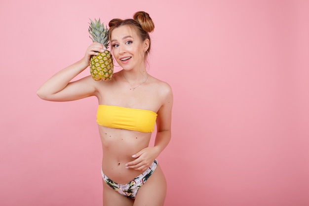 Girl in a yellow swimsuit and pineapple on a pink bright summer space