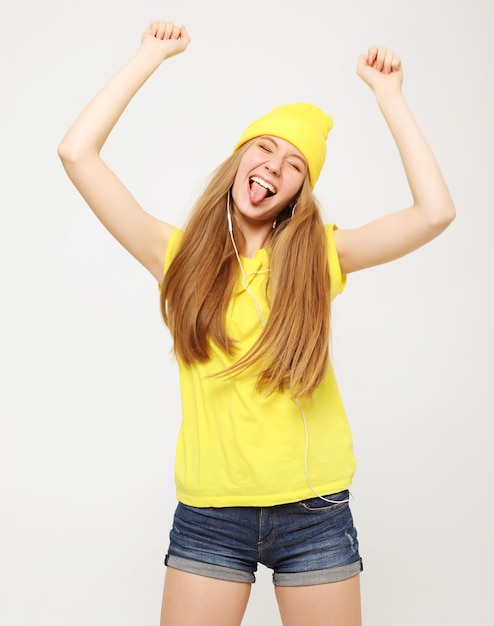 영감을 받은 얼굴 표정으로 춤추는 노란색 티셔츠를 입은 소녀 캐주얼 여름 복장을 한 활동적인 젊은 여성이 실내에서 즐거운 시간을 보내고 있습니다.