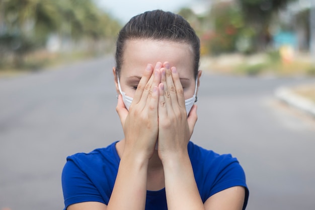 女の子、若い素敵な女性が通りで汚染された空気に苦しんでいる滅菌医療保護マスクを通して呼吸、隠れ、彼女の顔、手で目を覆っています。ドラマ、パンデミック中国コロナウイルスの概念