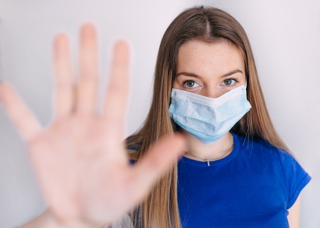 Girl, young woman in protective sterile medical mask on her face looking, hand, stop no sign. Air pollution, virus, Chinese pandemic coronavirus concept.