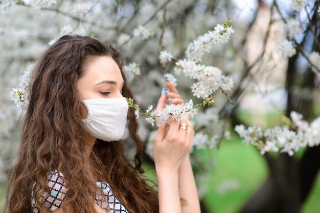 봄 정원에서 그녀의 얼굴에 보호 멸균 의료 마스크에 소녀, 젊은 여자. 대기 오염, 바이러스, 유행성 코로나 바이러스 개념.
