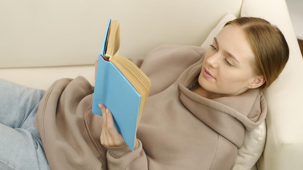 girl or young woman reading book lying down on sofa