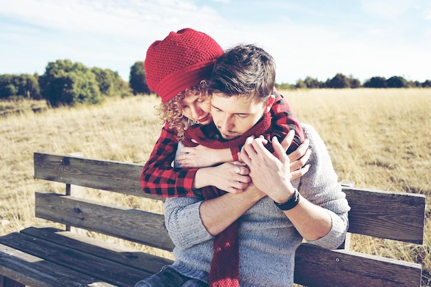 Girlfriend embracing boyfriend on bench during sunny day